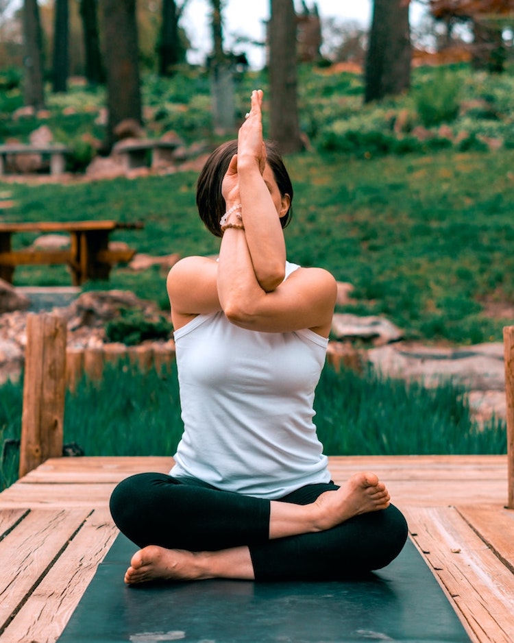 girl wearing white shirt doing twisted yoga pose on green yoga mat